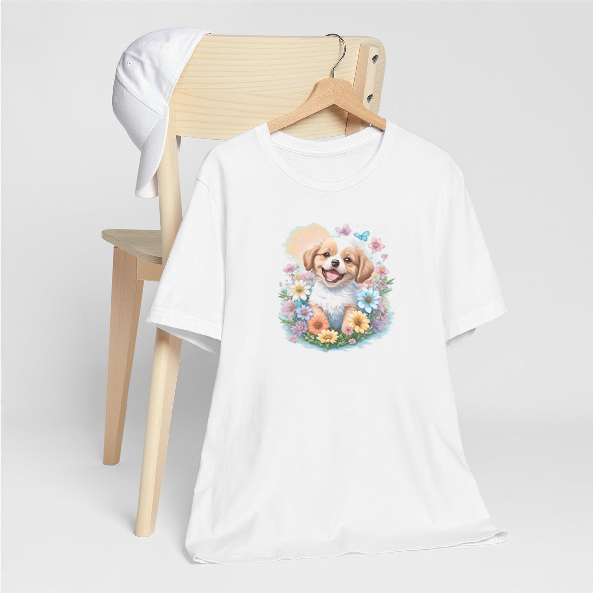 White crew neck short sleeved t-shirt, feature a graphic vibrant colorful hand-drawn dog face of a Shepherd Puppy sitting in floral wreath. T-shirt hanging on chair shown in close-up to highlight print and size