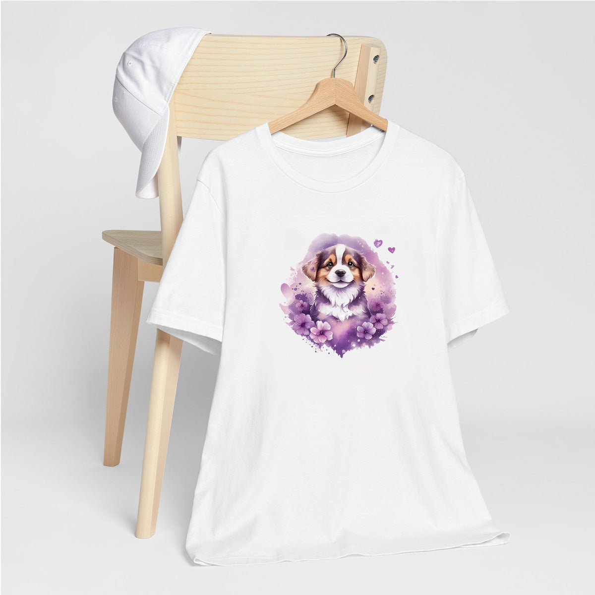 White crew neck short sleeved t-shirt, features an adorable Shepherd puppy, nestle in hearts and floral garden. T-shirt hanging on chair shown in close-up to highlight print and size