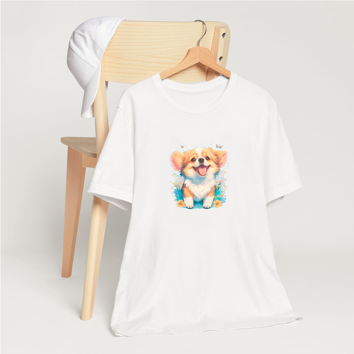 White crew neck short sleeved t-shirt,feature a graphic vibrant colorful hand-drawn dog face of a Corgi puppy sitting in floral garden. T-shirt hanging on chair shown in close-up to highlight print and size
