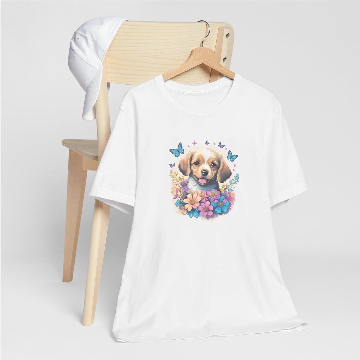 White crew neck short sleeved t-shirt, feature a graphic vibrant colorful hand-drawn dog face of a golden retriever puppy sitting in floral wreath. hanger on chair
