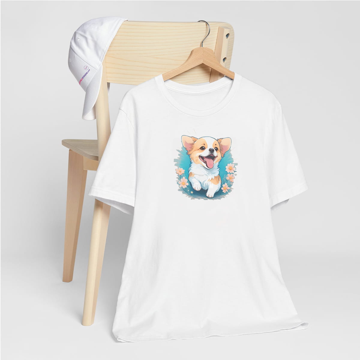 White crew neck short sleeved t-shirt, feature a graphic vibrant colorful hand-drawn Corgi puppy sitting in floral garden. T-shirt hanging on chair shown in close-up to highlight print and size