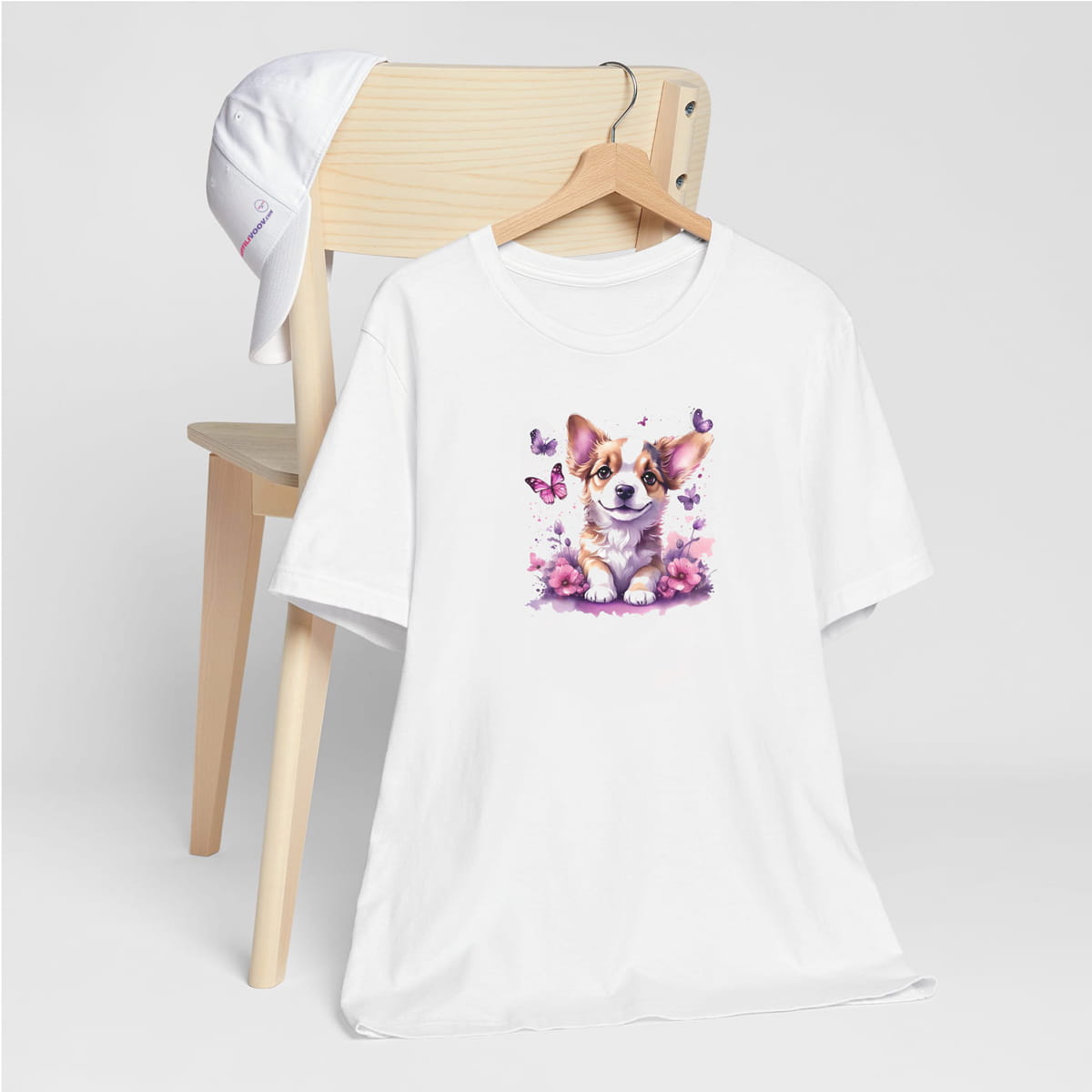 White crew neck short sleeved t-shirt, feature a graphic vibrant colorful hand-drawn Corgi puppy sitting in floral and butterfly garden. T-shirt hanging on chair shown in close-up to highlight print and size.