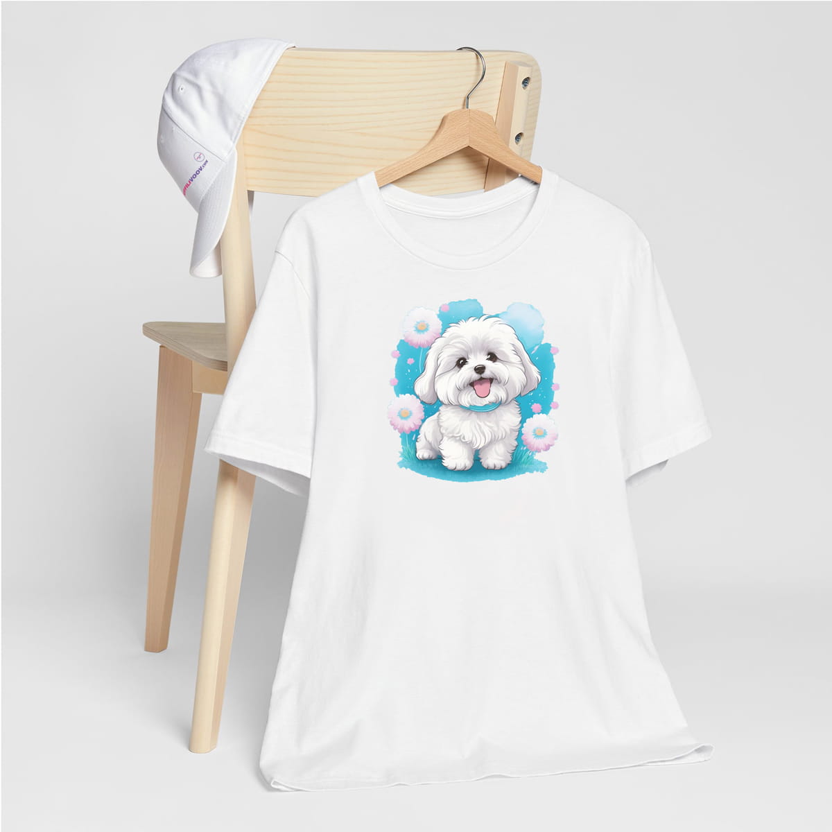 White crew neck short sleeve t-shirt with a colorful hand-drawn Coton de tulear puppy graphic standing in a floral garden. shirt hanging on chair, close up showing bold dog art, cute pet-themed fashion