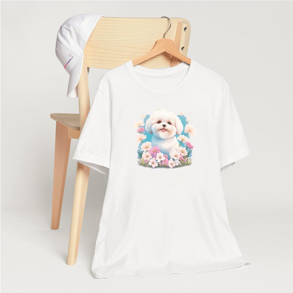 White crew neck short sleeve t-shirt with a colorful hand-drawn Coton de tulear puppy graphic sitting in a floral garden. shirt, hanging on a chair close up showing bold dog art, cute pet-themed fashion