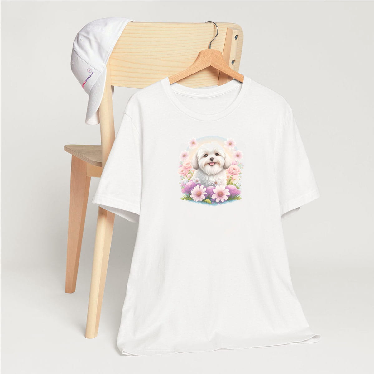 White crew neck short sleeve t-shirt with a colorful hand-drawn Coton de tulear puppy graphic sitting in a floral garden. shirt, hanging on a chair close up showing bold dog art, cute pet-themed fashion