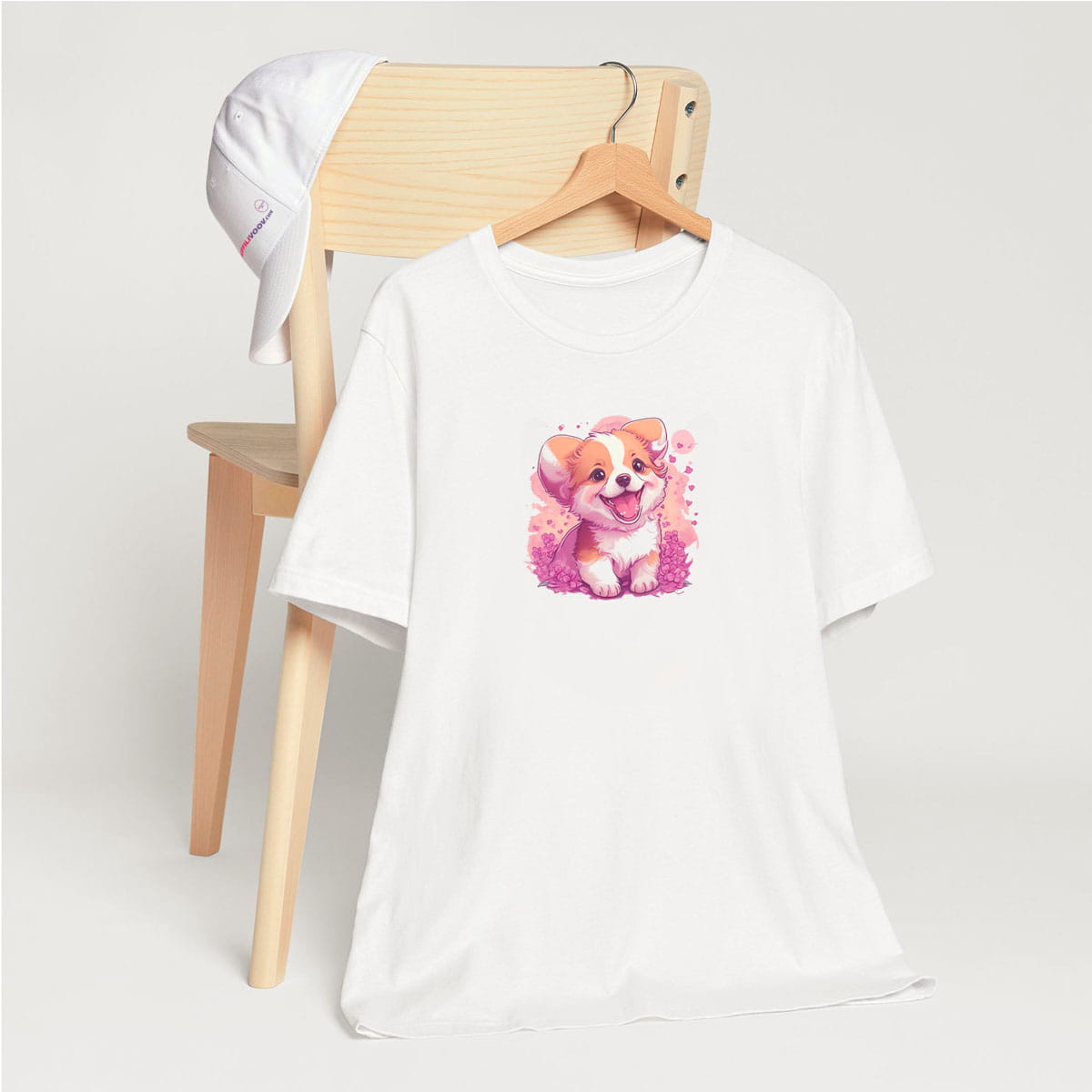 White crew neck short sleeved t-shirt, feature a graphic vibrant colorful hand-drawn puppy dog face in vibrant purple/pink hue palette in a floral garden. T-shirt hanging on chair shown in close-up to highlight print and size.