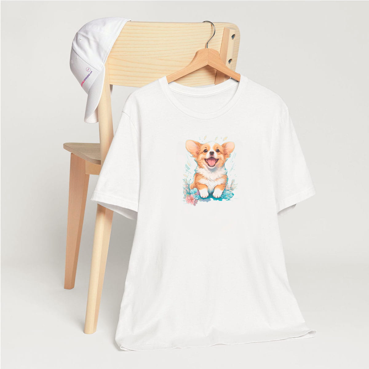 White crew neck short sleeved t-shirt, feature a graphic vibrant colorful hand-drawn corgi puppy standing, happy face in vibrant palette in a floral garden. T-shirt hanging on chair shown in close-up to highlight print and size