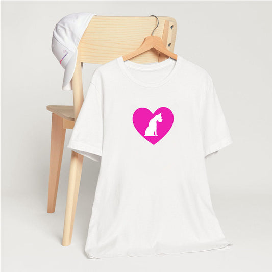 White crew neck short sleeved t-shirt, feature a graphic hand-drawn sitting dog in a nestle of pink heart. T-shirt hanging on chair shown in close-up to highlight print and size