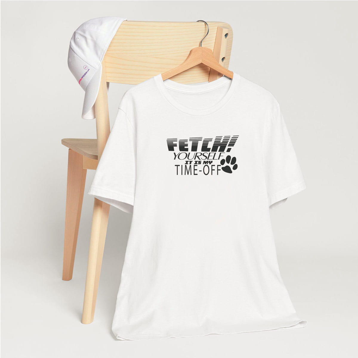 White crew neck short sleeved t-shirt, feature a fun statement, quote Fetch yourself it is my time-off. T-shirt hanging on chair shown in close-up to highlight print and size