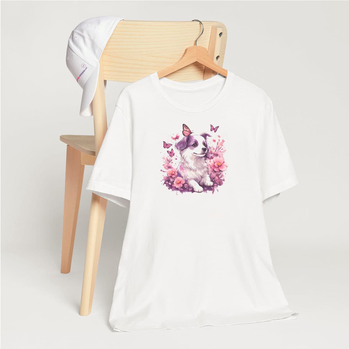 White crew neck short sleeved t-shirt, featuring an adorable, lovable puppy nestled amidst a blooming floral spectacle within a quaint wicker basket. T-shirt hanging on chair shown in close-up to highlight print and size