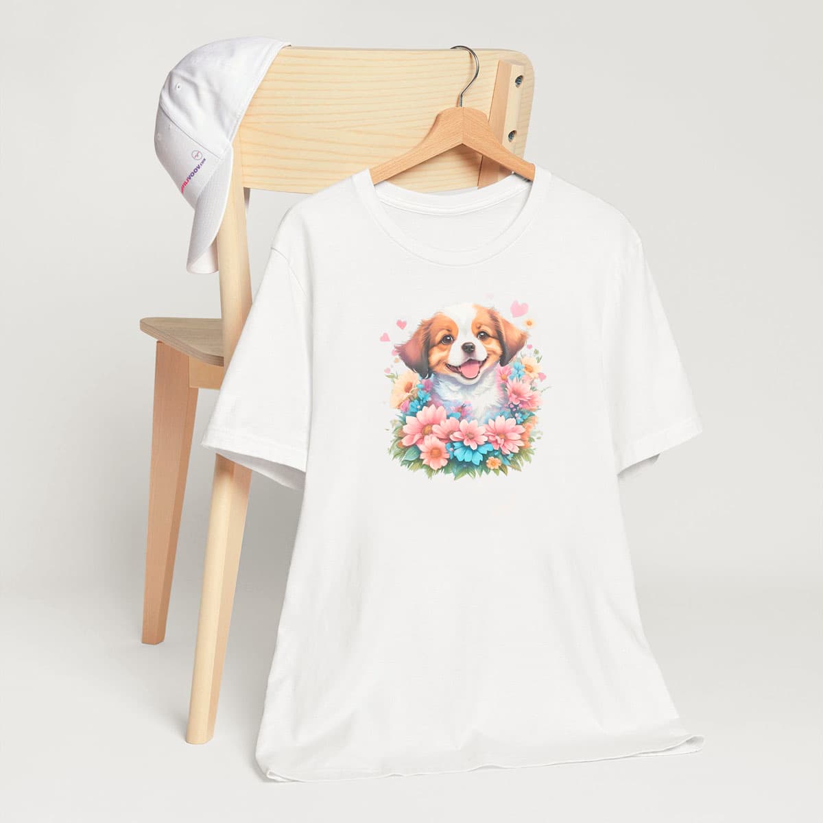 White crew neck short sleeved t-shirt, showcases an adorable Australian shepherd pup amidst a floral fiesta. T-shirt hanging on chair shown in close-up to highlight print and size