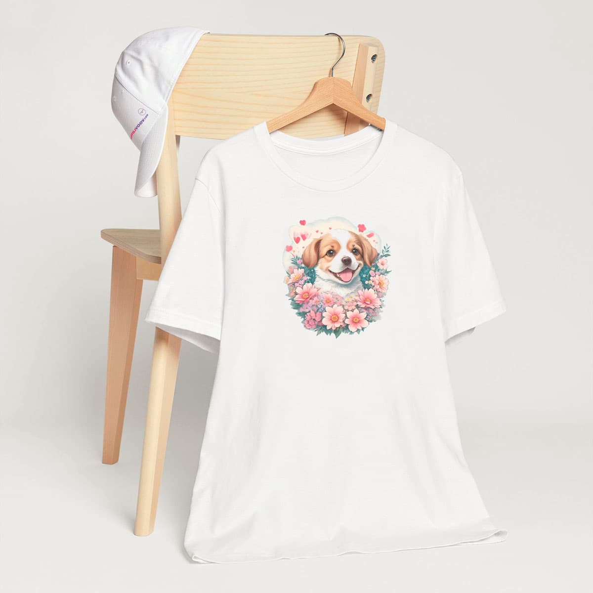 White crew neck short sleeved t-shirt, Showcases an adorable happy Spaniel pup, nestled among a bloom-filled wicker basket. T-shirt hanging on chair shown in close-up to highlight print and size
