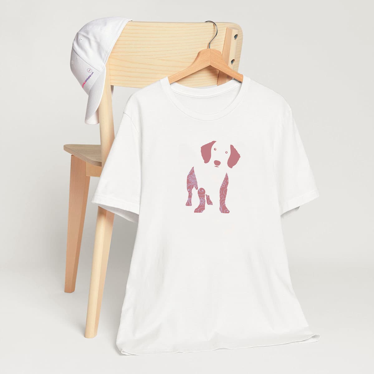 White crew neck short sleeved t-shirt, feature a Dachshund silhouette with floral and swirl pattern design in vibrant colors. T-shirt hanging on chair shown in close-up to highlight print and size
