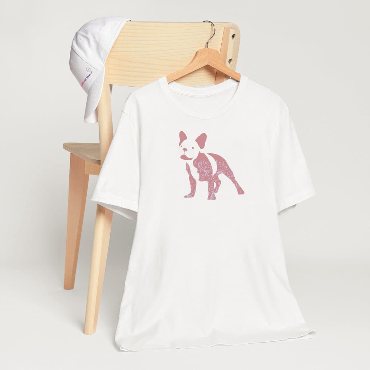 White crew neck short sleeved t-shirt, features a charming bulldog silhouette with floral, and swirl pattern design. T-shirt hanging on chair shown in close-up to highlight print and size