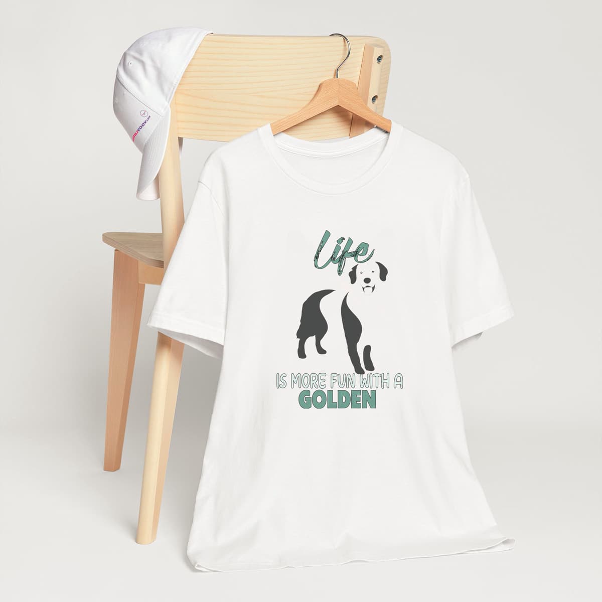 White unisex short sleeved cotton t-shirt showing Golden retriever silhouette and “Life is more fun with a golden” quote printed across the chest. model tee hanging on a chair
