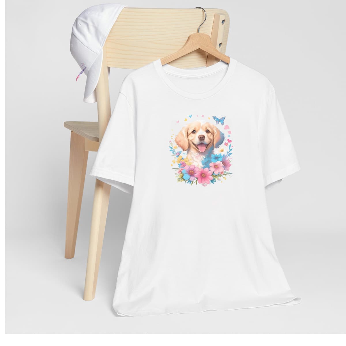 White crew neck short sleeved t-shirt, feature a happy Golden Retriever puppies cute dog face nestle with butterflies and floral basket. T-shirt hanging on chair shown in close-up to highlight print and size
