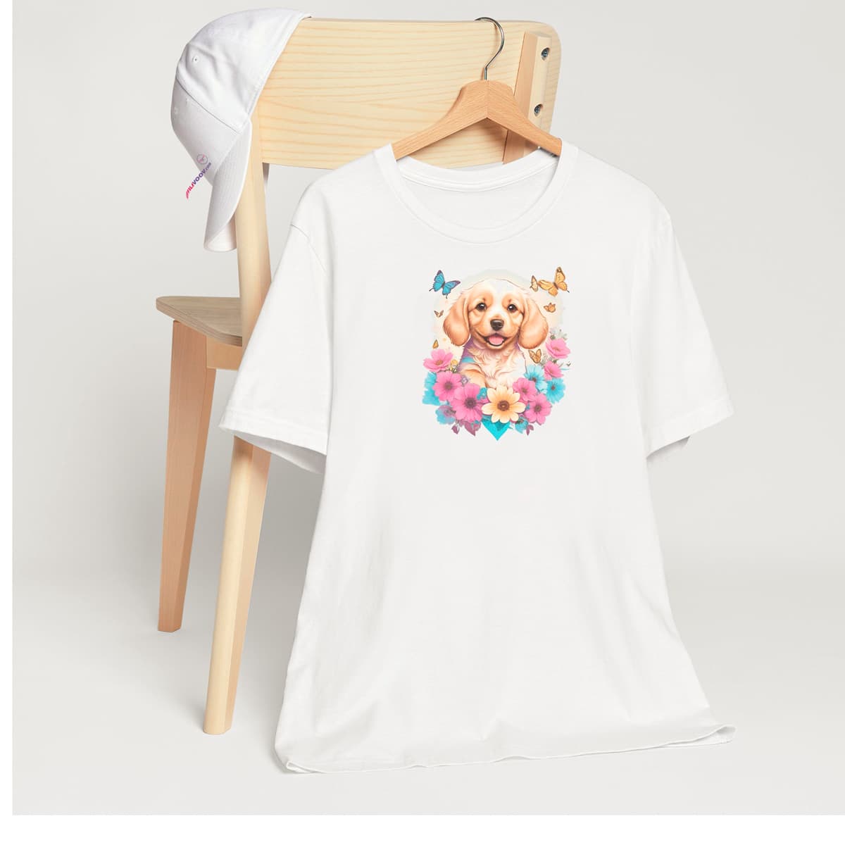 White crew neck short sleeved t-shirt, feature a happy Golden Retriever puppy dog face, surrounded by a floral symphony within a wicker basket. T-shirt hanging on chair shown in close-up to highlight print and size