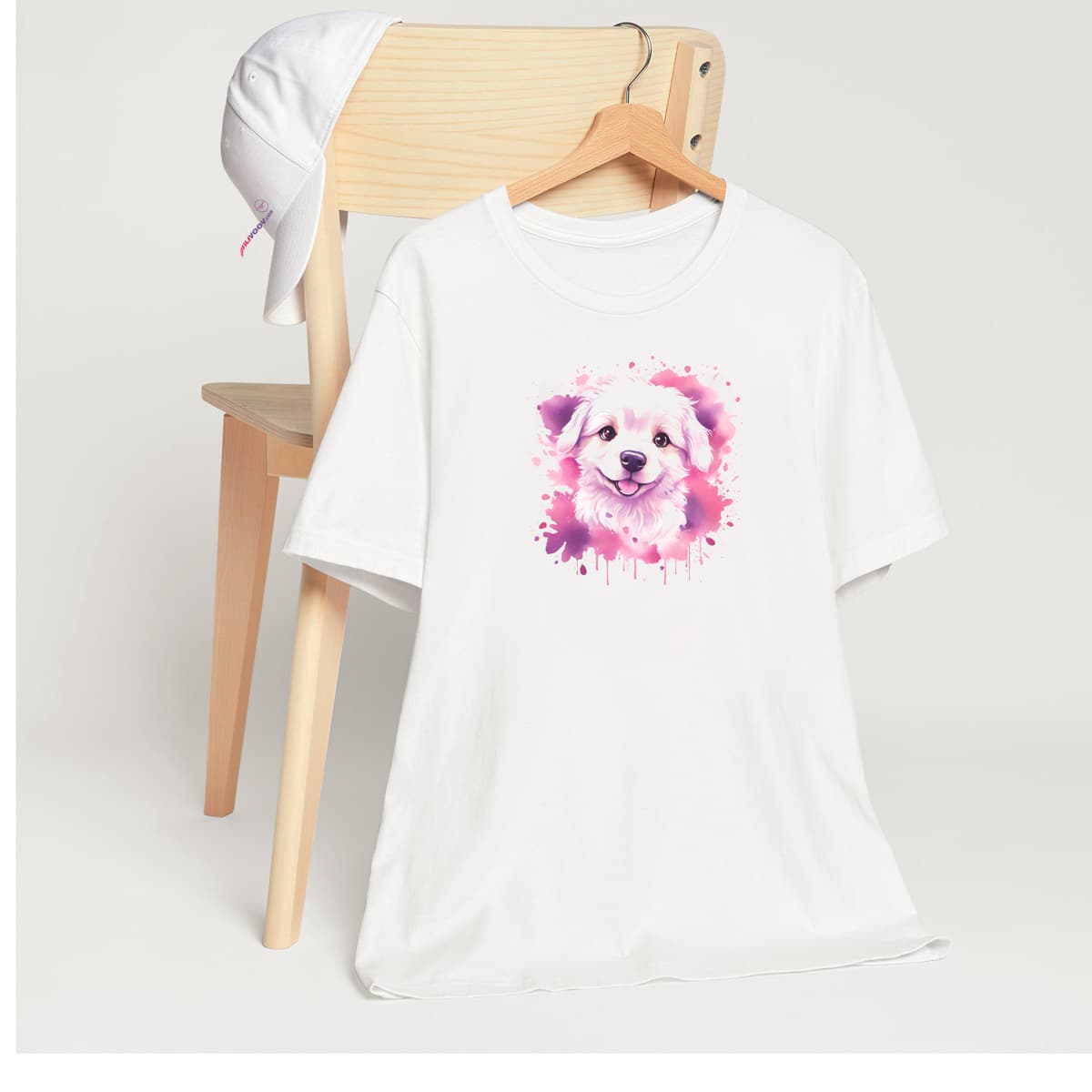 White crew neck short sleeved t-shirt. Featuring an enchanting Maltese puppy amidst a tapestry of splash artistry in vibrant pink and purple toned colors. T-shirt hanging on chair shown in close-up to highlight print and size