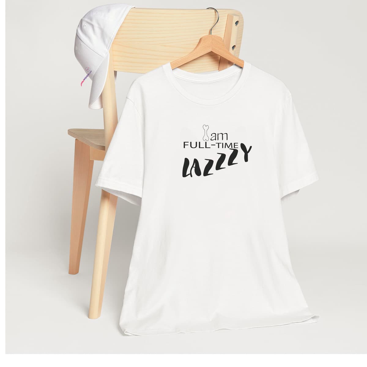 White crew neck short sleeved t-shirt, feature a graphic fun message ”I Am Full-time  Lazzzy”- seen from the dogs point of view.T-shirt hanging on chair shown in close-up to highlight print and size