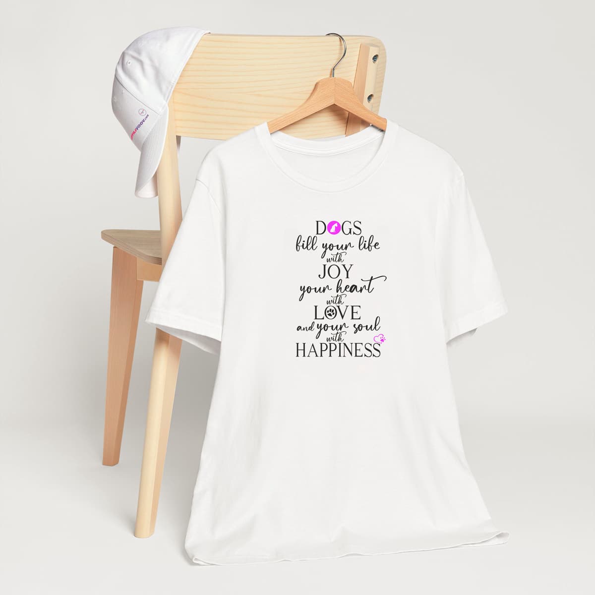 White crew neck short sleeved t-shirt. Featuring an inspiring dog quote" dogs fills your life with joy, your heart with love and your soul with happiness" in a black bold black text with a pink dog icon, heart, and paws.T-shirt hanging on chair shown in close-up to highlight print and size