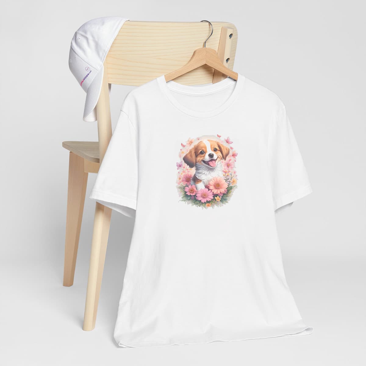 White crew neck short sleeved t-shirt, feature an adorable Shep puppy, nestled within a wicker basket brimming with a vibrant floral symphony and playful butterflies. T-shirt hanging on a chair, shown in close-up to highlight print and fit.