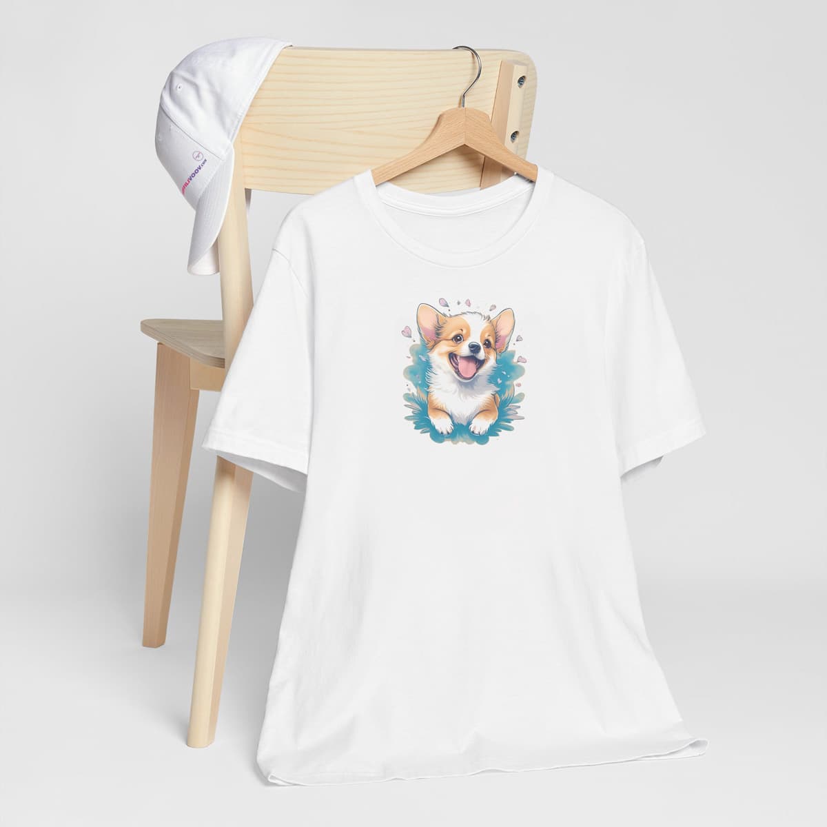 White crew neck short sleeved t-shirt, boasts an intricate and colorful cute Corgi puppy, nestle in floral garden. T-shirt hanging on chair shown in close-up to highlight print and size