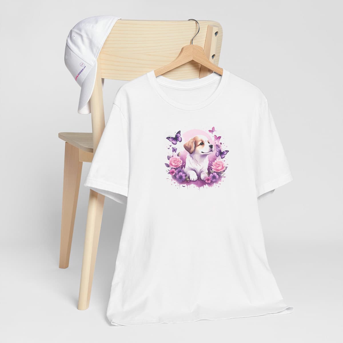 White crew neck short sleeved t-shirt, showcase an adorable puppy nestled amidst a vibrant floral basket. T-shirt hanging on chair shown in close-up to highlight print and size