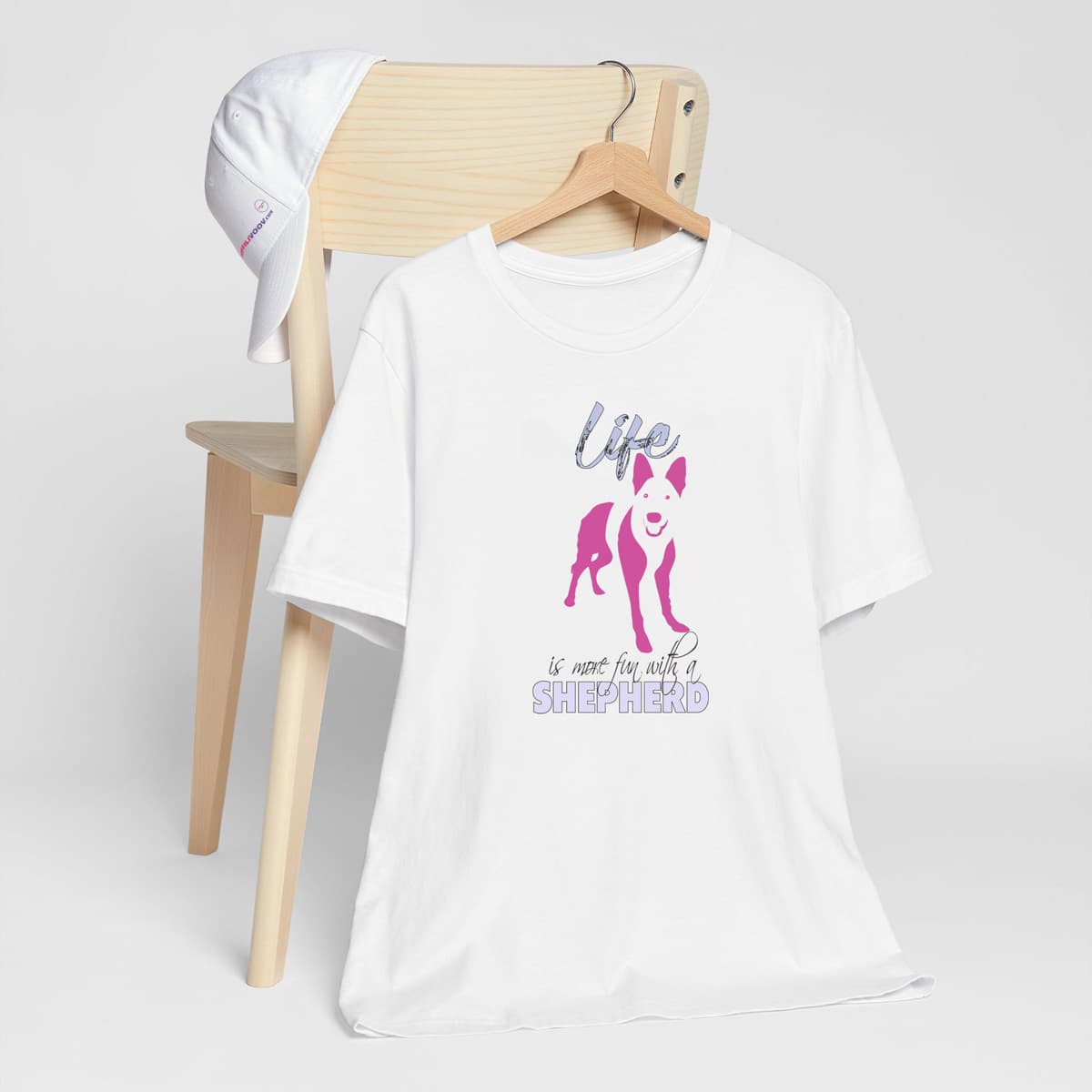 White crew neck short sleeved t-shirt. Feature a cute German Shepherd puppy silhouette with a fun message "life is more fun with a Shepherd"in pink and purple shades.T-shirt hanging on chair shown in close-up to highlight print and size.