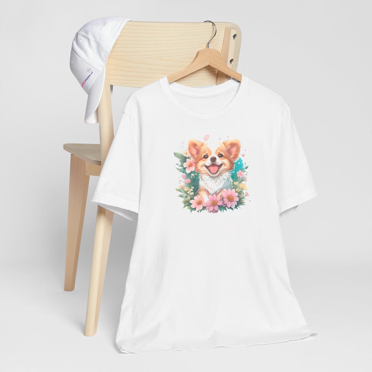 White crew neck short sleeved t-shirt, feature an intricate colorful hand-drawn lively shepherd puppy amidst a blooming wicker floral basket garden. T-shirt hanging on chair shown in close-up to highlight print and size