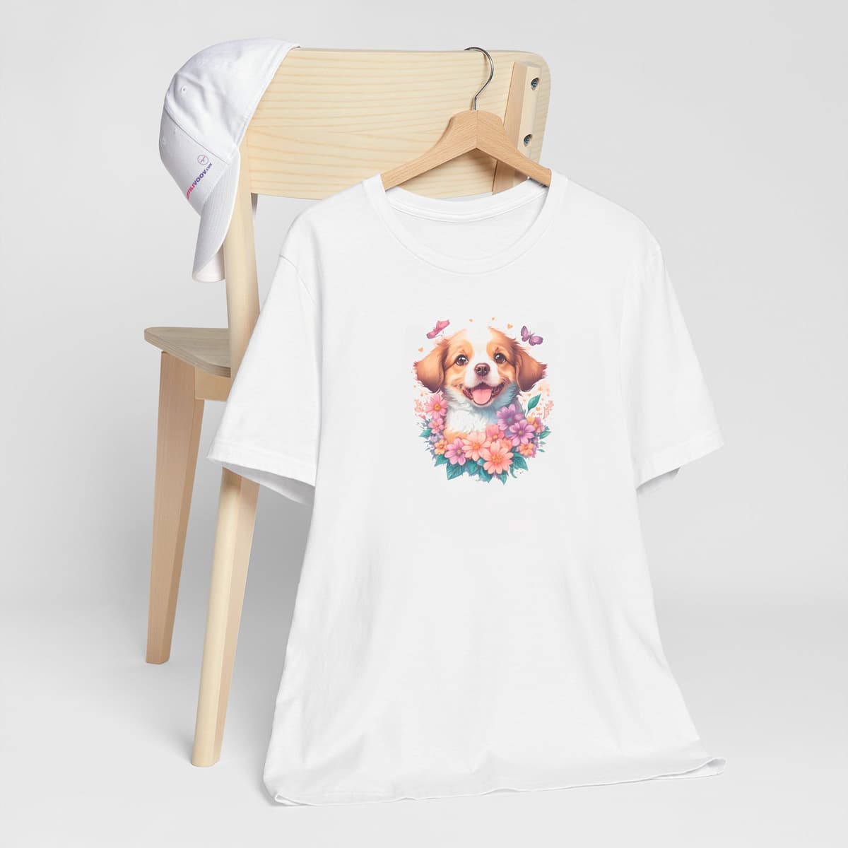 White crew neck short sleeved t-shirt, feature an intricate colorful hand-drawn lively shepherd puppy amidst a blooming wicker floral basket garden. T-shirt hanging on chair shown in close-up to highlight print and size