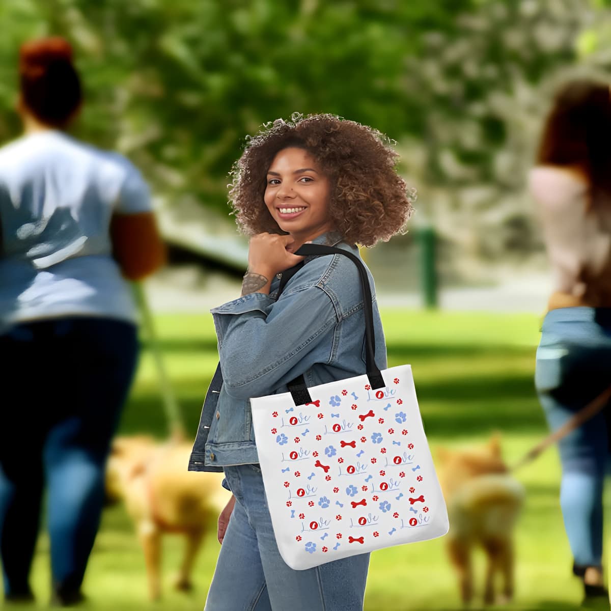 Young woman standing in a park, carrying on her shoulder a white tote polyester canvas bag, with black stripped handle, feature a striking black handle striping and an eye-catching graphic of playful dog bones, paws, and the word "love," with a sitting dog as the logo.