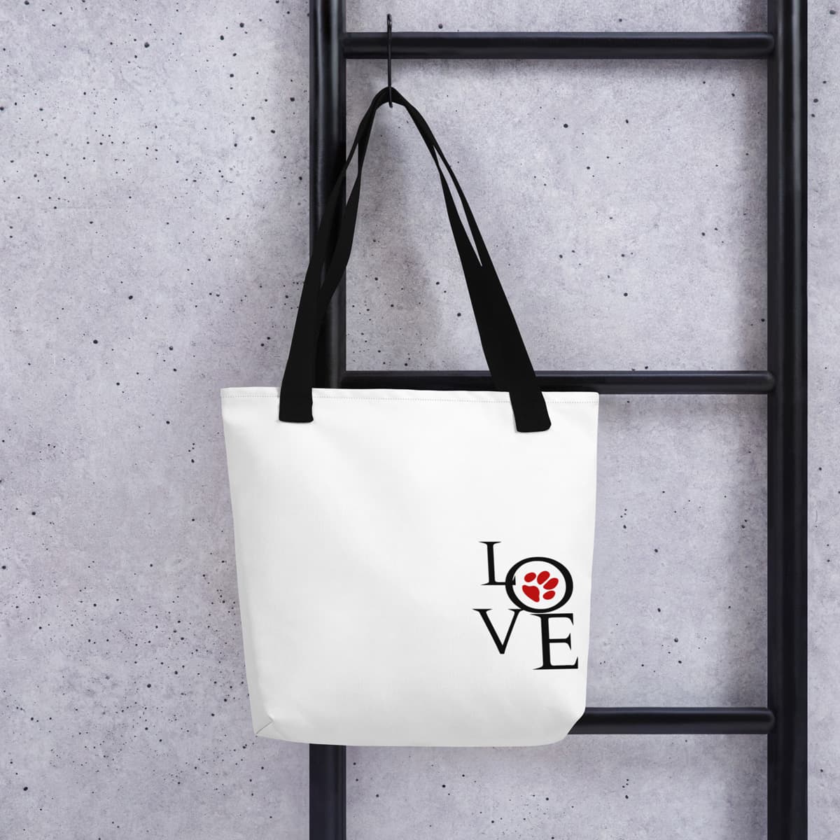 Hanging on a hook a Uni-size 15"x15" white tote polyester canvas bag, with black stripped handle, featuring an artistry graphic ”LOVE” with a cute red dog paw in the letter ”o”.
