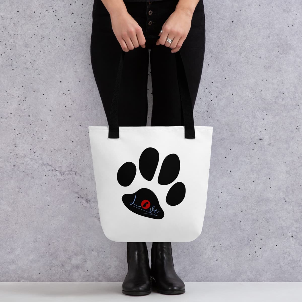 Female model holding a Uni-size 15"x15" white tote polyester canvas bag, with black stripped handle, feature a black one-line large paw print, underlay by bold LOVE with a cute silhouette dog in the ”o” in red color.