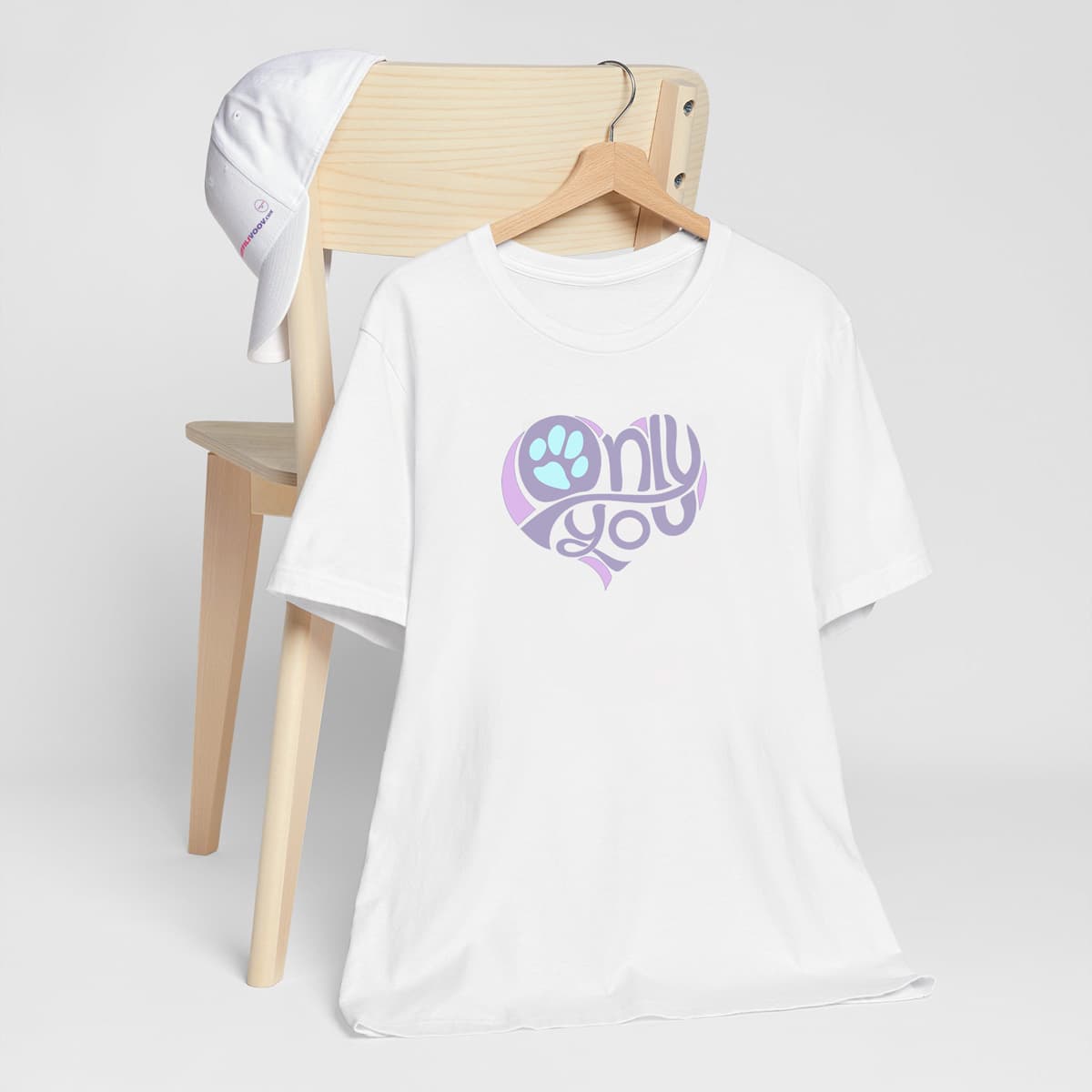 Hanging on a chair a unisex short sleeve crew neck t-shirt in white, featuring a bold ‘Only You’ text with a purple graphic, pink heart, and turquoise paw print. Soft cotton, cozy fit, stylish apparel for dog moms, pet lovers, and everyday casual wear.