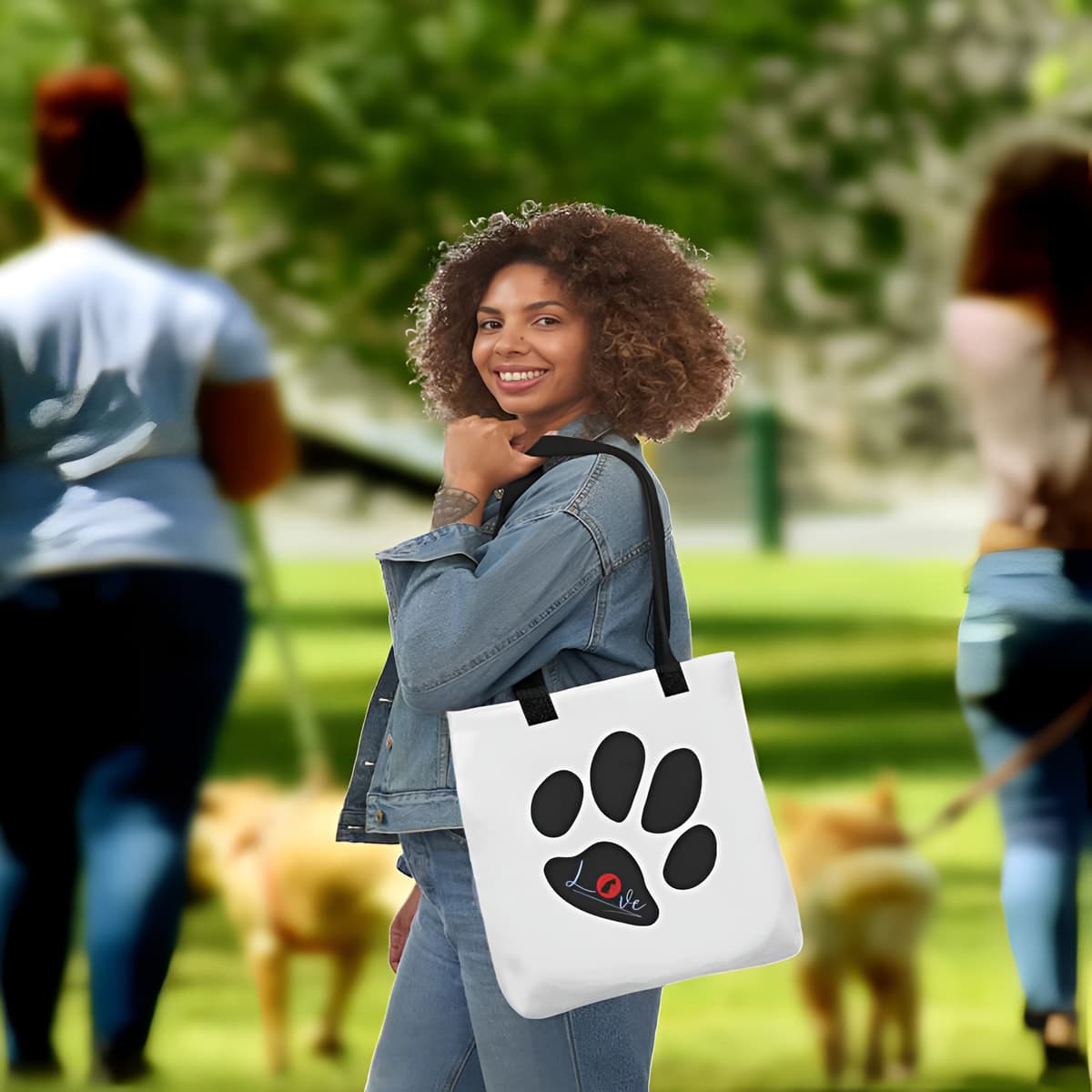 Young women standing in a park, on her shoulder is a white tote polyester canvas bag, with black stripped handle, feature a black one-line large paw print, underlay by bold LOVE with a cute silhouette dog in the ”o” in red color.