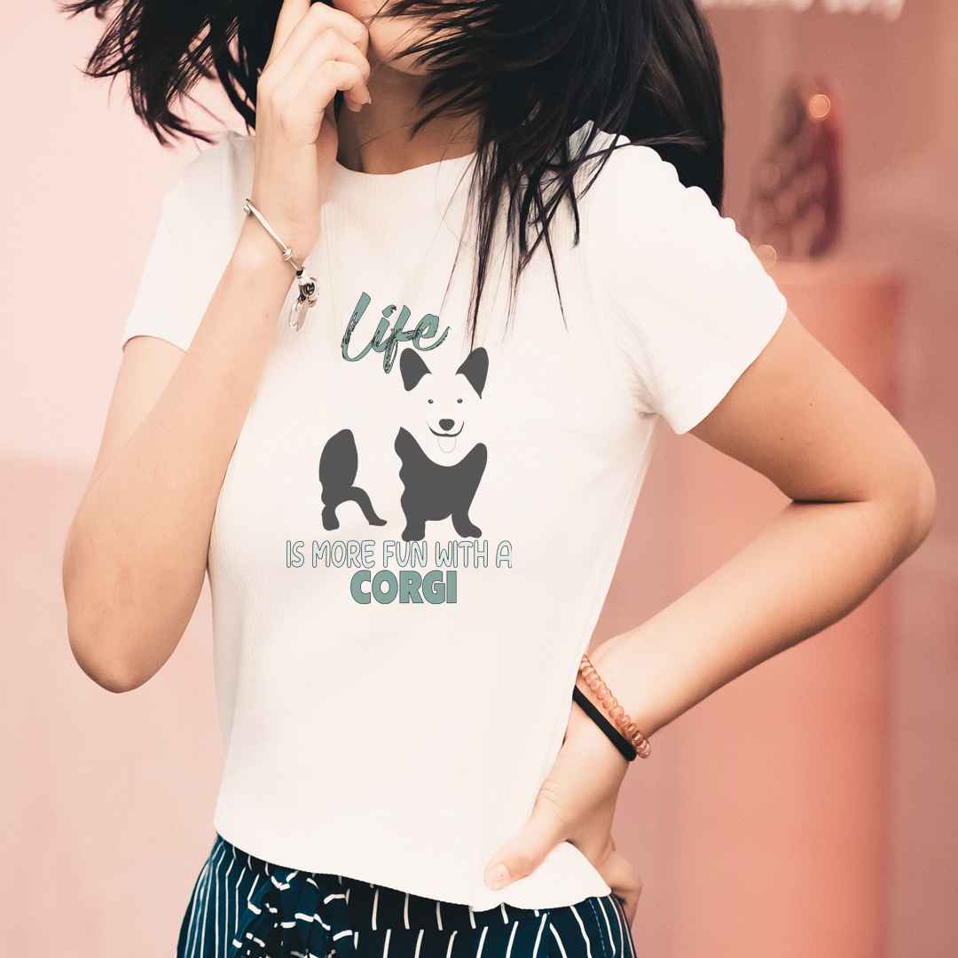 Women standing, wearing a white crew neck short sleeved t-shirt, features a classic quote "life is more fun wit a Corgi, feature a cute standing corgi in black/white bold one-line graphic.