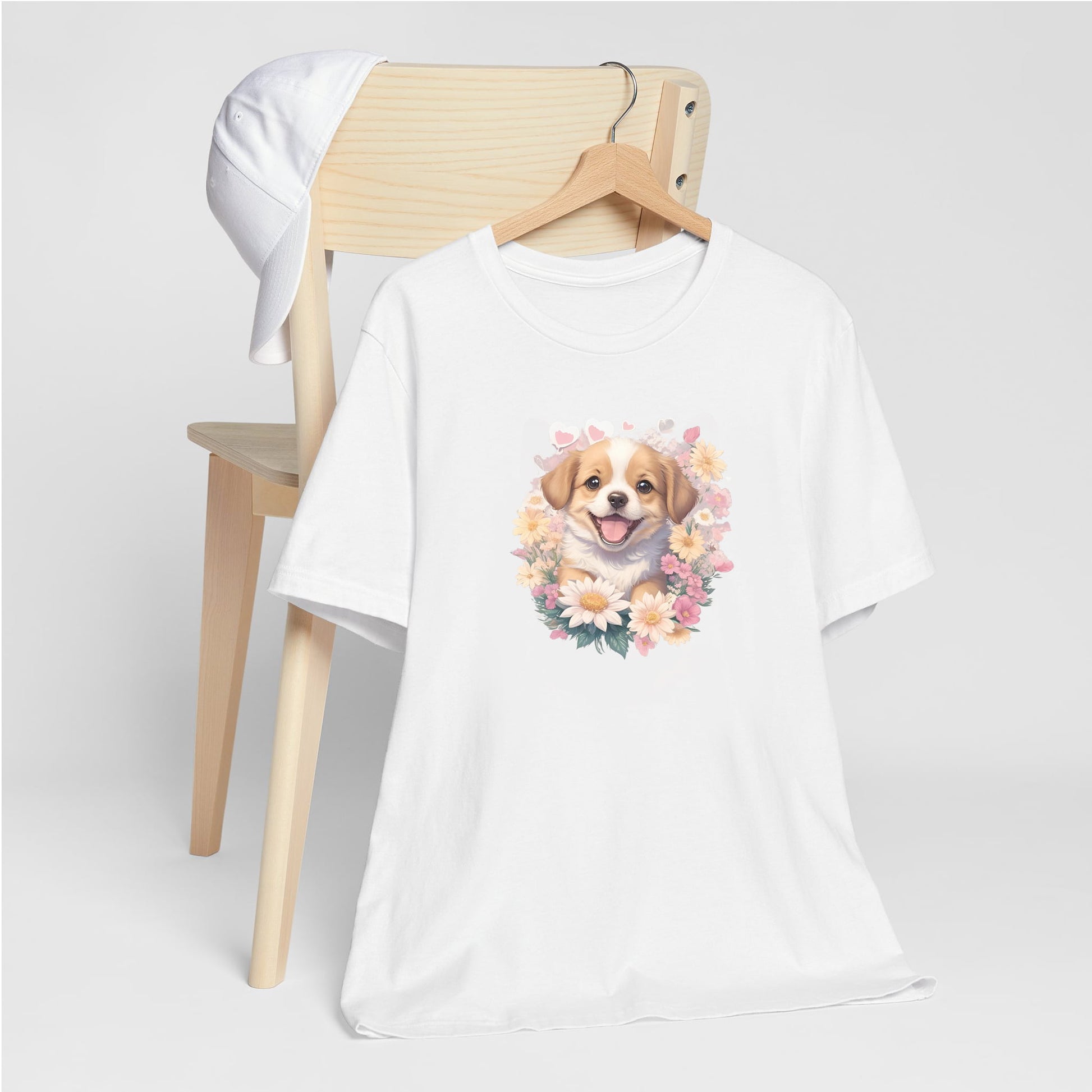 White crew neck short sleeved t-shirt, feature a graphic vibrant colorful hand-drawn dog face of a  Cavalier King Charles spaniel Puppy sitting in floral wreath. hanger on chair