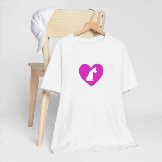 White crew neck short sleeved t-shirt, feature a graphic hand-drawn sitting dog in a nestle of pink heart. T-shirt hanging on chair shown in close-up to highlight print and size