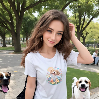 Women standing in a dog park, with two dogs. She is wearing a white crew neck short sleeved t-shirt, feature a graphic vibrant colorful hand-drawn dog face of a Shepherd Puppy sitting in floral wreath. 
