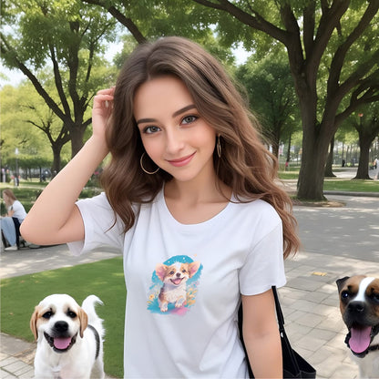 Women standing in a park, with two dogs. She is wearing a crisp white crew neck short sleeved t-shirt,features a graphic vibrant colorful hand-drawn dog face of a cute Corgi puppy sitting in floral garden.