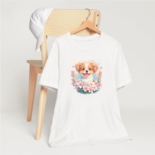 White crew neck short sleeved t-shirt, showcases an Australian shepherd puppy, radiating cuteness like the sun's embrace, nestled amidst a blossoming floral fiesta within a wicker embrace. T-shirt hanging on chair shown in close-up to highlight print and size