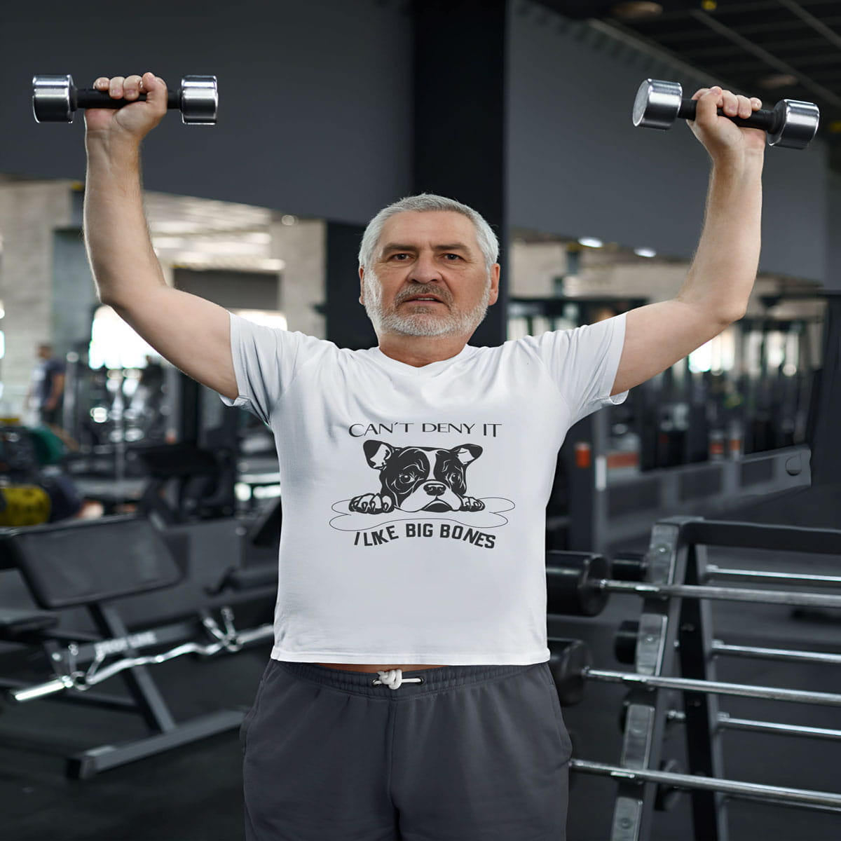 Man wearing a white crew neck short sleeved t-shirt, feature a graphic black/white hand-drawn cute bulldog face protecting its dog bone. Man model wearing shirt white working out in the gym