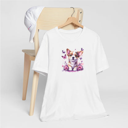 White crew neck short sleeved t-shirt, feature a graphic vibrant colorful hand-drawn Corgi puppy sitting in floral and butterfly garden. T-shirt hanging on chair shown in close-up to highlight print and size.