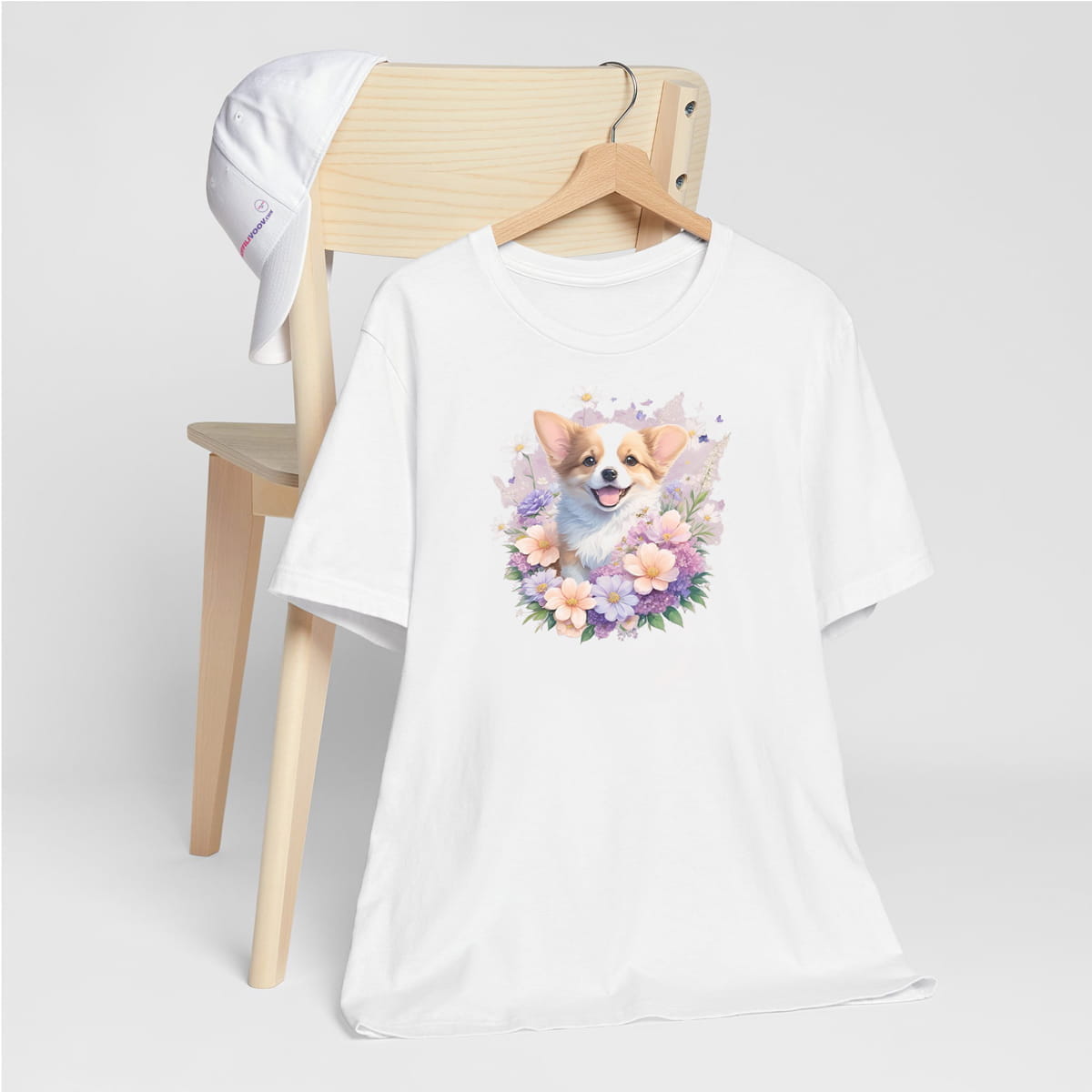 White crew neck short sleeve t-shirt with a colorful hand-drawn Corgi puppy graphic sitting in a floral garden.  shirt, hanging on a chair showing bold dog art, cute pet-themed fashion