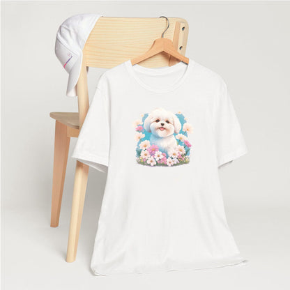 White crew neck short sleeve t-shirt with a colorful hand-drawn Coton de tulear puppy graphic sitting in a floral garden. shirt, hanging on a chair close up showing bold dog art, cute pet-themed fashion
