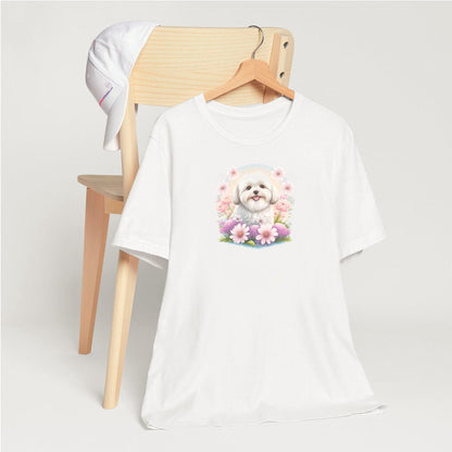 White crew neck short sleeve t-shirt with a colorful hand-drawn Coton de tulear puppy graphic sitting in a floral garden.  shirt,  hanging on a chair close up showing bold dog art, cute pet-themed fashion