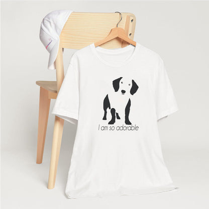 White crew neck short sleeved t-shirt, feature a feature a standing dachshund in black/white silhouette with quote "I am so adorable".  T-shirt hanging on chair shown in close-up to highlight print and size
