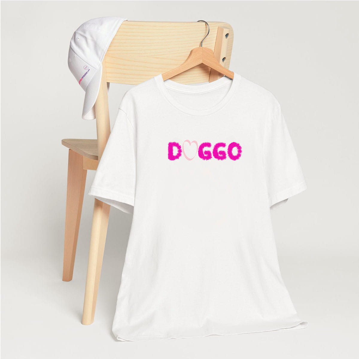 
White crew neck short sleeved t-shirt, features a fluffy purple outline "DOGGO"and a cute pink heart. T-shirt hanging on chair shown in close-up to highlight print and size
