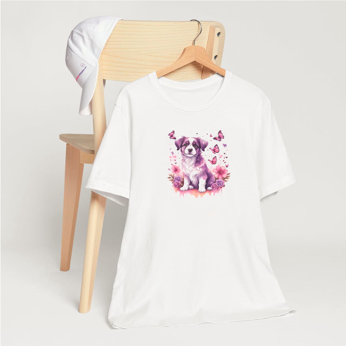 White crew neck short sleeved t-shirt, feature a tapestry of colors and a joyful cute puppy nestle in butterflies and floral garden. T-shirt hanging on chair shown in close-up to highlight print and size.
