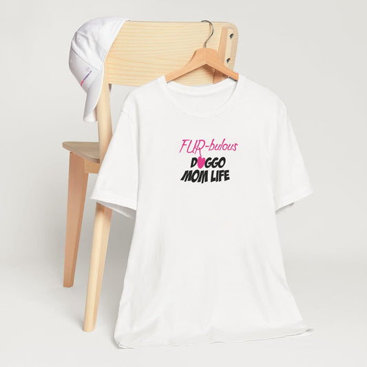 White crew neck short sleeved t-shirt. Featuring a pink "Fur-bulous and Doggo Mom life with cute pink heart graphic style, fits true to sizes. T-shirt hanging on chair shown in close-up to highlight print and size.